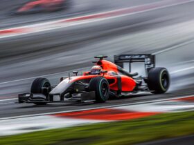 Egy vörös-fekete Formula–1-es versenyautó nagy sebességgel száguld a pályán, a háttér elmosódása hangsúlyozza a mozgás és az adrenalin intenzitását.